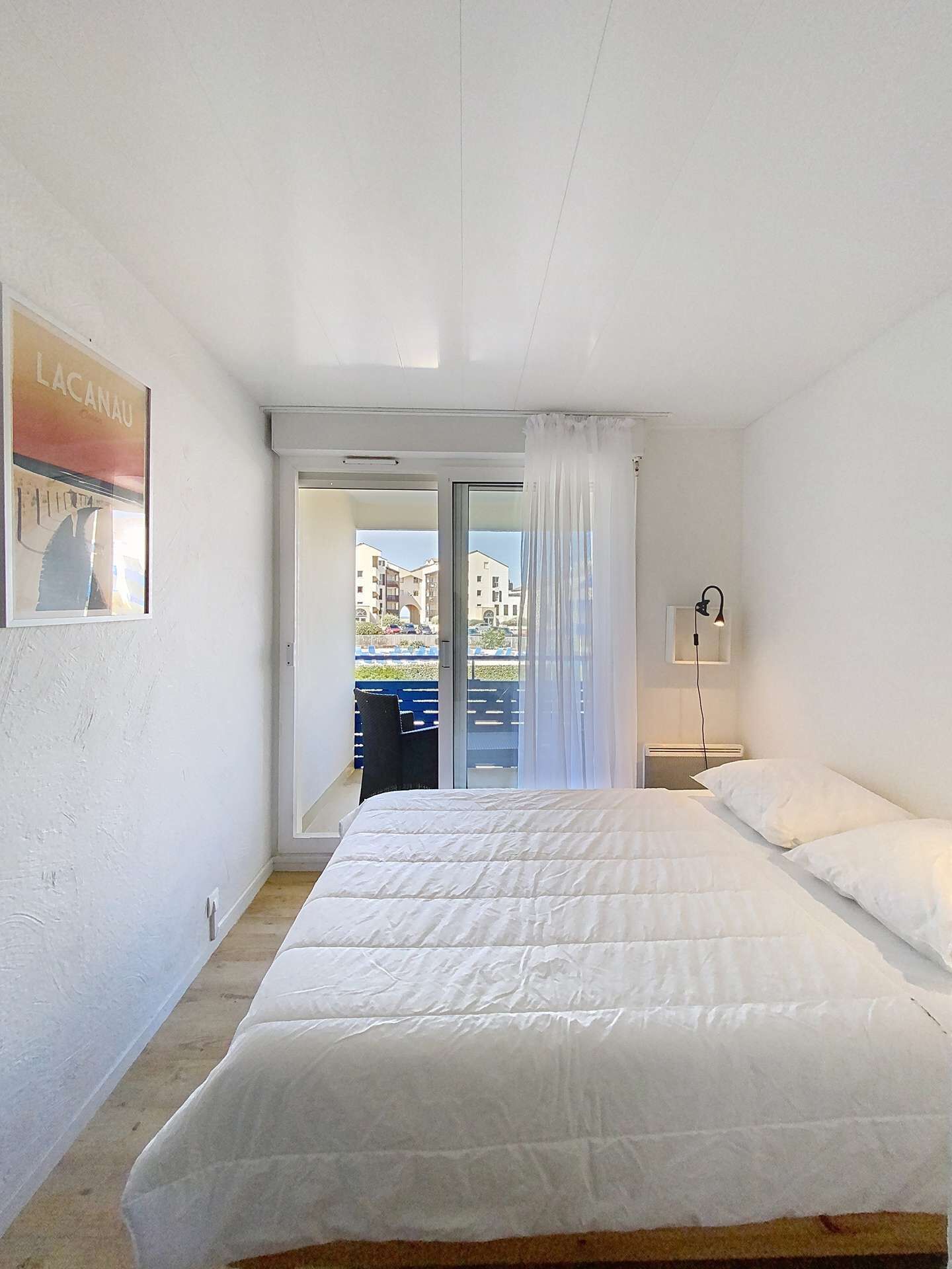 Une chambre avec un grand lit, une table de chevet, une lampe et une vue sur le balcon extérieur.