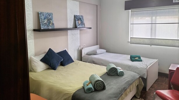 Une chambre d’hôtel avec deux lits simples, un ventilateur de plafond, une fenêtre avec des stores et une petite table.