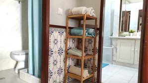 Une salle de bain avec des toilettes blanches, une étagère en bois où sont posées des serviettes et un mur orné d’un motif.