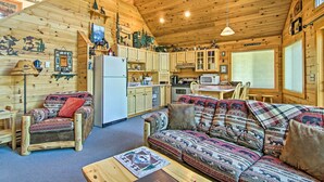 A cozy cabin interior with wooden walls, a sofa, a chair, a dining table, and a kitchen area. - Florissant Hilltop Hideaway w/ Porch, Pond View (Florissant)