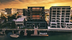 Un edificio moderno de varios pisos con un muelle y barcos, que cuenta con balcones y ventanas amplias.