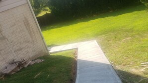 A concrete pathway leading to a house with a brick wall.