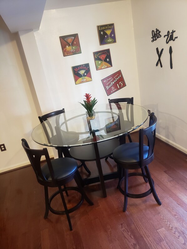 A dining area with a glass-top table, four chairs, and wall art including a Budweiser sign.