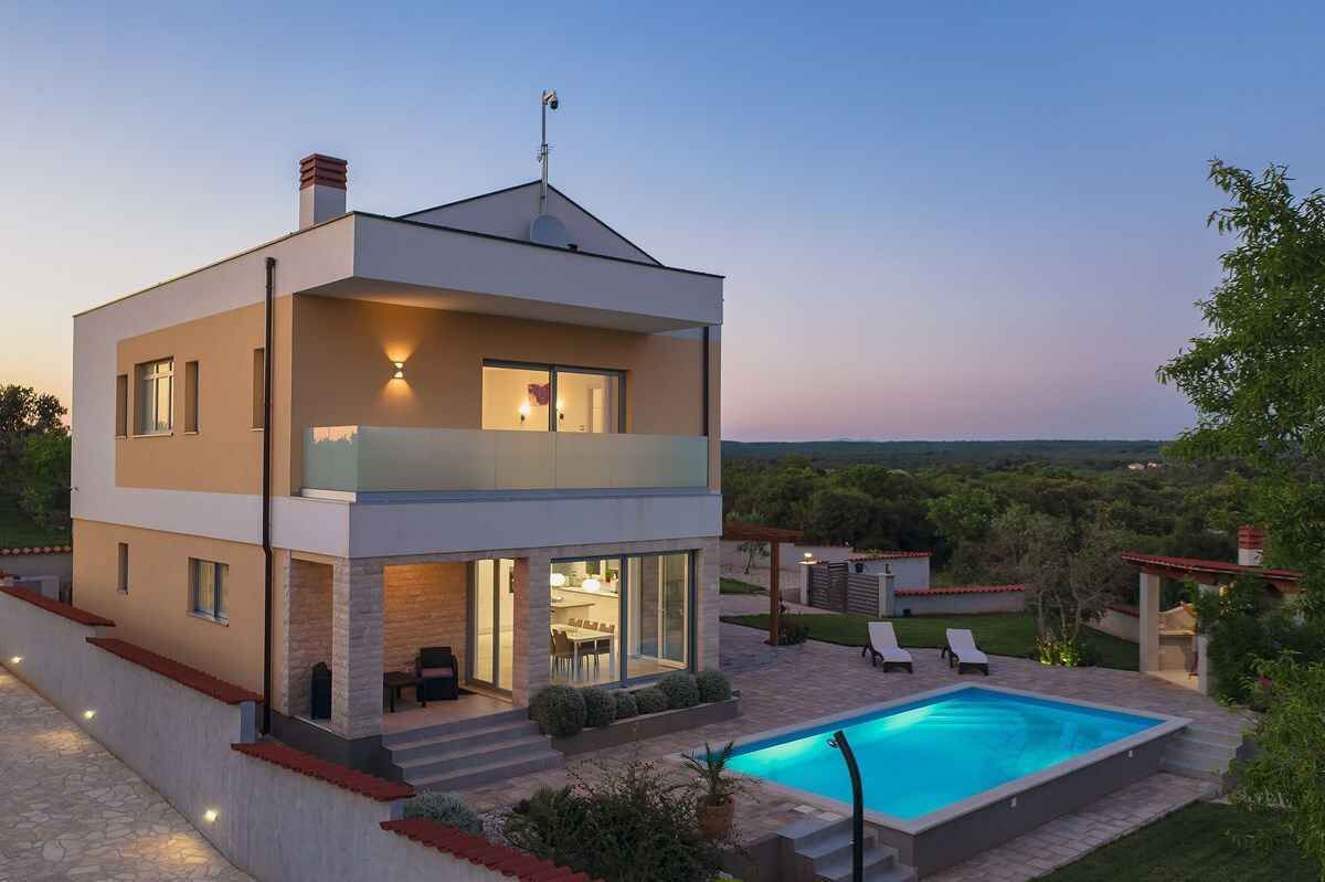 Une maison moderne à deux étages, dotée d’une piscine, d’un espace de détente extérieur et offrant une vue sur le paysage.