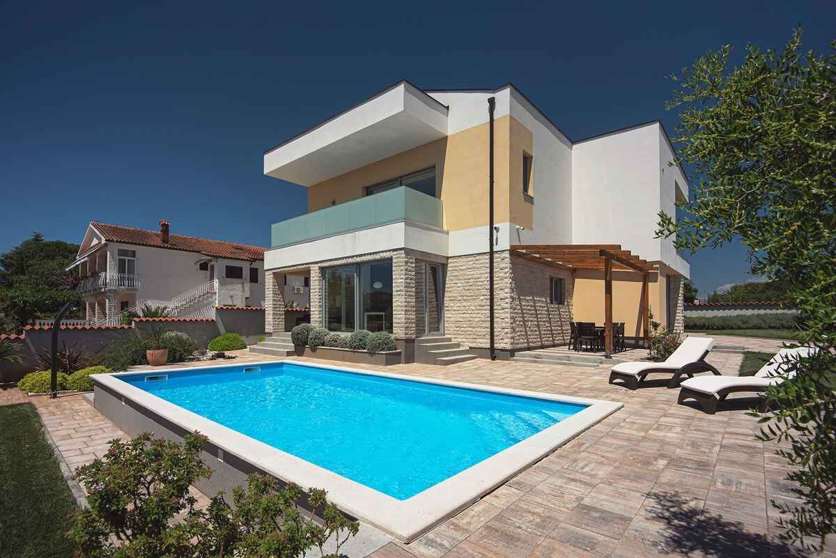 Une maison moderne à deux étages, dotée d’une piscine et d’un espace extérieur aménagé pour se détendre.