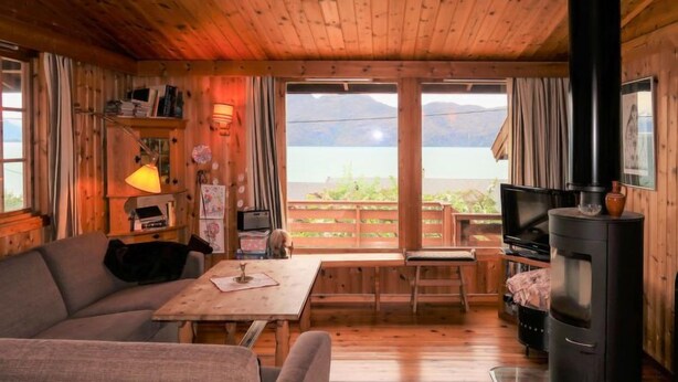 Een gezellig interieur van een blokhut met een bank, een tafel, een televisie en een houtkachel.