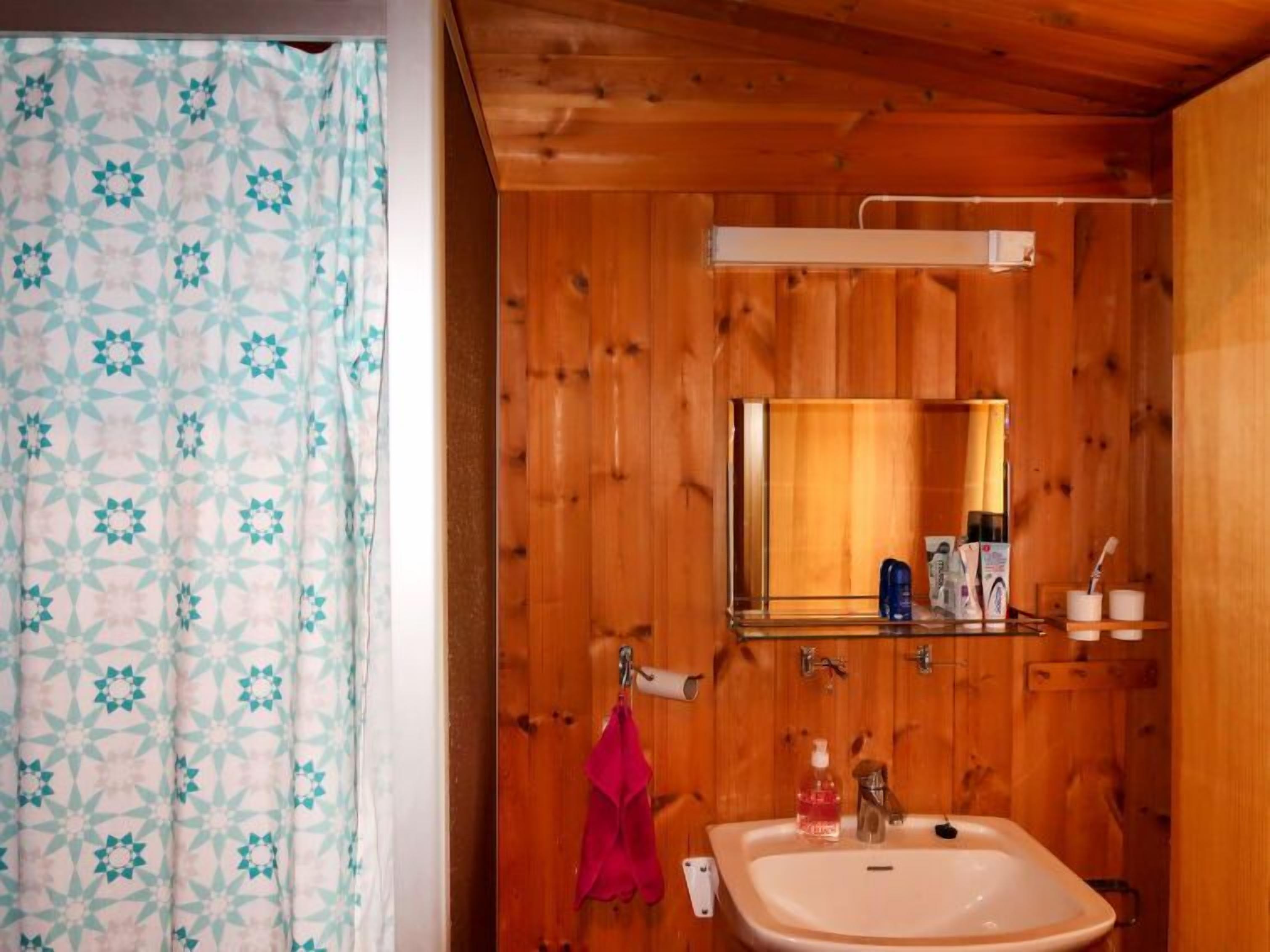 Een badkamer met houten lambrisering, een wastafel, spiegel en een handdoek aan de muur.
