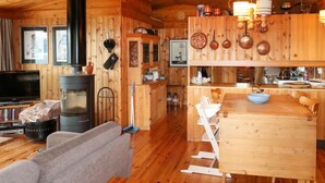 Een gezellig chaletinterieur met een houtkachel, een eethoek en een woonkamer met een bank en televisie.