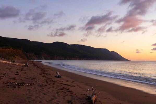 Una playa con cielo despejado, mar tranquilo y colinas a lo lejos.