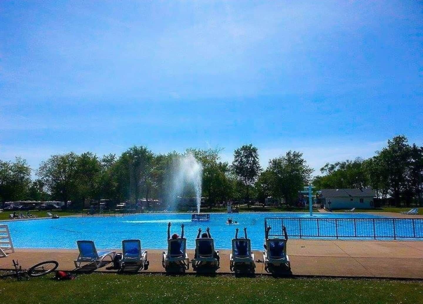 A swimming pool with a water fountain, surrounded by lounge chairs and a grassy area.