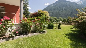 A hotel with a garden featuring pink flowers and a mountain view. - Large appartment with big garden, ideal for families! (Molini di Tures)