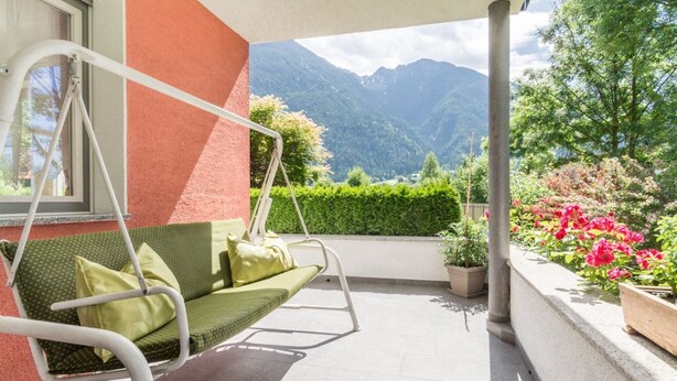A balcony with a swing chair, potted plants, and a view of mountains. - Large appartment with big garden, ideal for families! (Molini di Tures)