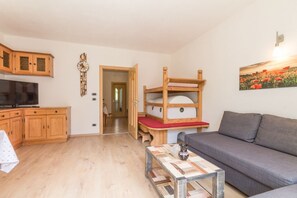 Un espacio habitable compacto con sofá, televisión, armarios de madera, una cama litera y un cuadro en la pared.