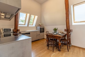 Une cuisine moderne avec un coin repas, des chaises en bois, un îlot central et une vue sur l’extérieur grâce à de grandes fenêtres.