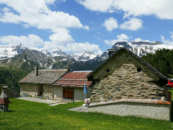 A stone building with a sloped roof, a chimney, and a door with a wooden shutter.