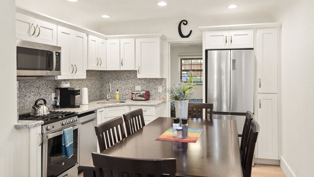 A modern kitchen with white cabinets, stainless steel appliances, and a central island with seating. - Beaver Street Cottage w/AC, Fully Fenced Yard, W/D, 4 Smart TVs, Speedy Wi-Fi. (Flagstaff)