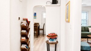 A hallway with a bookshelf, a dining area, and a living room with a sofa and a table. - Beaver Street Cottage w/AC, Fully Fenced Yard, W/D, 4 Smart TVs, Speedy Wi-Fi. (Flagstaff)