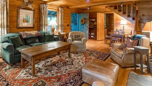 Un accogliente interno di una baita in legno con un divano verde, una poltrona bianca, un tavolino in legno e un tappeto decorato.
