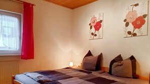 A bedroom with a wooden bed, a window with red curtains, and two wall-mounted flower paintings.