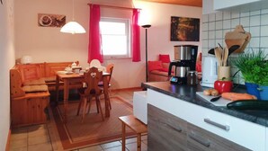 A cozy kitchen with wooden cabinets, a dining area with a wooden table and chairs, and a window with red curtains.