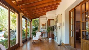 A spacious room with wooden flooring, large windows, a ceiling with exposed beams, a white armchair, a floor lamp, and a bookshelf. - Spectacular finca with pool in the outskirts of Inca (Inca)