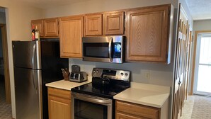 Una cocina con gabinetes de madera, un refrigerador de acero inoxidable, un microondas, un tostador y un horno.