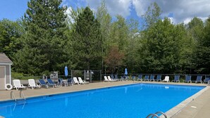 Una piscina rectangular con agua azul cristalina, rodeada de sillas reclinables blancas y sombrillas azules.