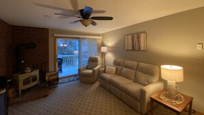 Una sala de estar con chimenea, ventilador de techo, sofá, sillón y lámpara.
