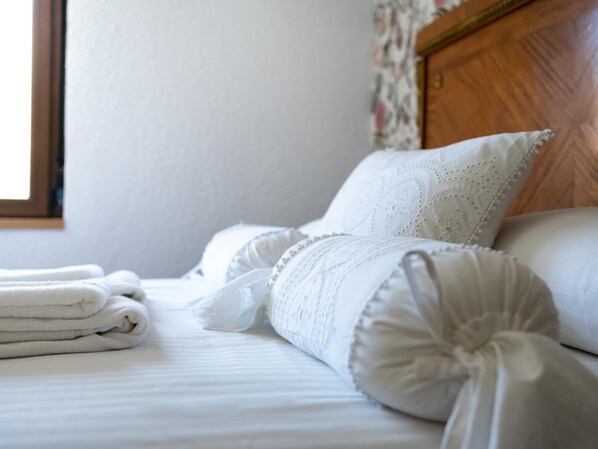 A neatly made bed with white linens and decorative pillows, a wooden headboard, and a window with a view of the outside. - -Housing León- Gaudí Attic (León)