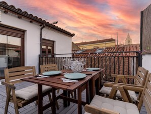 A wooden deck with a table set for two, overlooking a cityscape with a church spire. - -Housing León- Gaudí Attic (León)