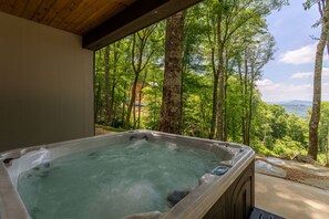 A hot tub with a view of a forested area and mountains in the distance.