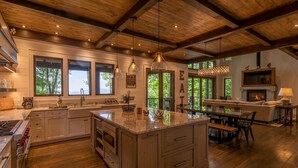 A spacious kitchen with a large island, wooden ceiling beams, and a fireplace. - Timber Forge Lodge - Eagles Nest home with views, hot tub, game table, more! (Banner Elk)