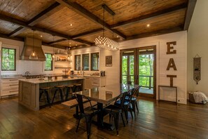A spacious kitchen with a large island, wooden ceiling beams, and a dining area with a glass table and chairs.