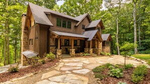 A large, multi-story wooden house with a stone foundation, surrounded by a forest. - Timber Forge Lodge - Eagles Nest home with views, hot tub, game table, more! (Banner Elk)