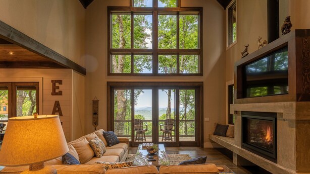 A spacious living room with a large window, a fireplace, and a cozy seating area. - Timber Forge Lodge - Eagles Nest home with views, hot tub, game table, more! (Banner Elk)