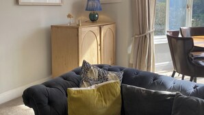 A living room with a dark-colored sofa, a wooden cabinet, and a table with chairs. - Seaside 2-Bed,  Sleeps 4, Parking & Pet Friendly (Salcombe)