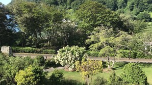 A lush garden with stone pathways, a variety of trees, and a stone wall. - Seaside 2-Bed,  Sleeps 4, Parking & Pet Friendly (Salcombe)
