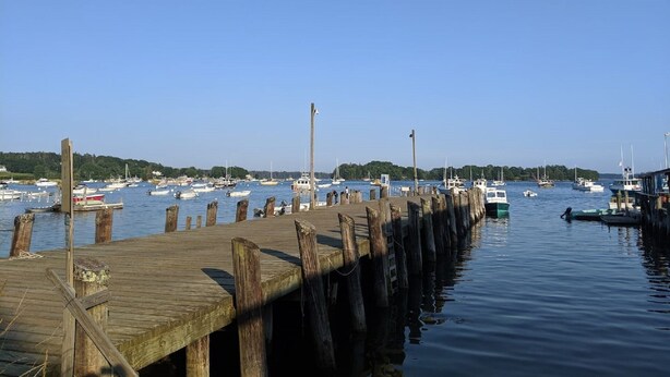 A wooden pier extending into calm water with several boats docked at the end. - Jameson Point Cottage in Scenic Friendship, Me (Friendship)