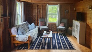 A cozy cabin interior with a sofa, two armchairs, a small table, and a television on a cabinet. - Jameson Point Cottage in Scenic Friendship, Me (Friendship)