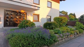 Una casa de dos pisos con fachada de piedra, una puerta principal de madera con paneles de vidrio y un jardín bien cuidado con arbustos y lavanda.