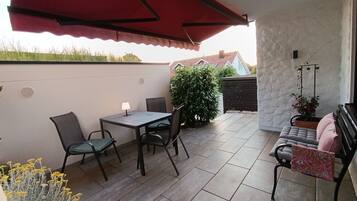 A patio with a table and chairs, a red awning, a potted plant, and a sofa.