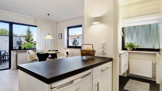 Una cocina moderna con encimera negra, armarios blancos y un comedor con mesa y sillas.