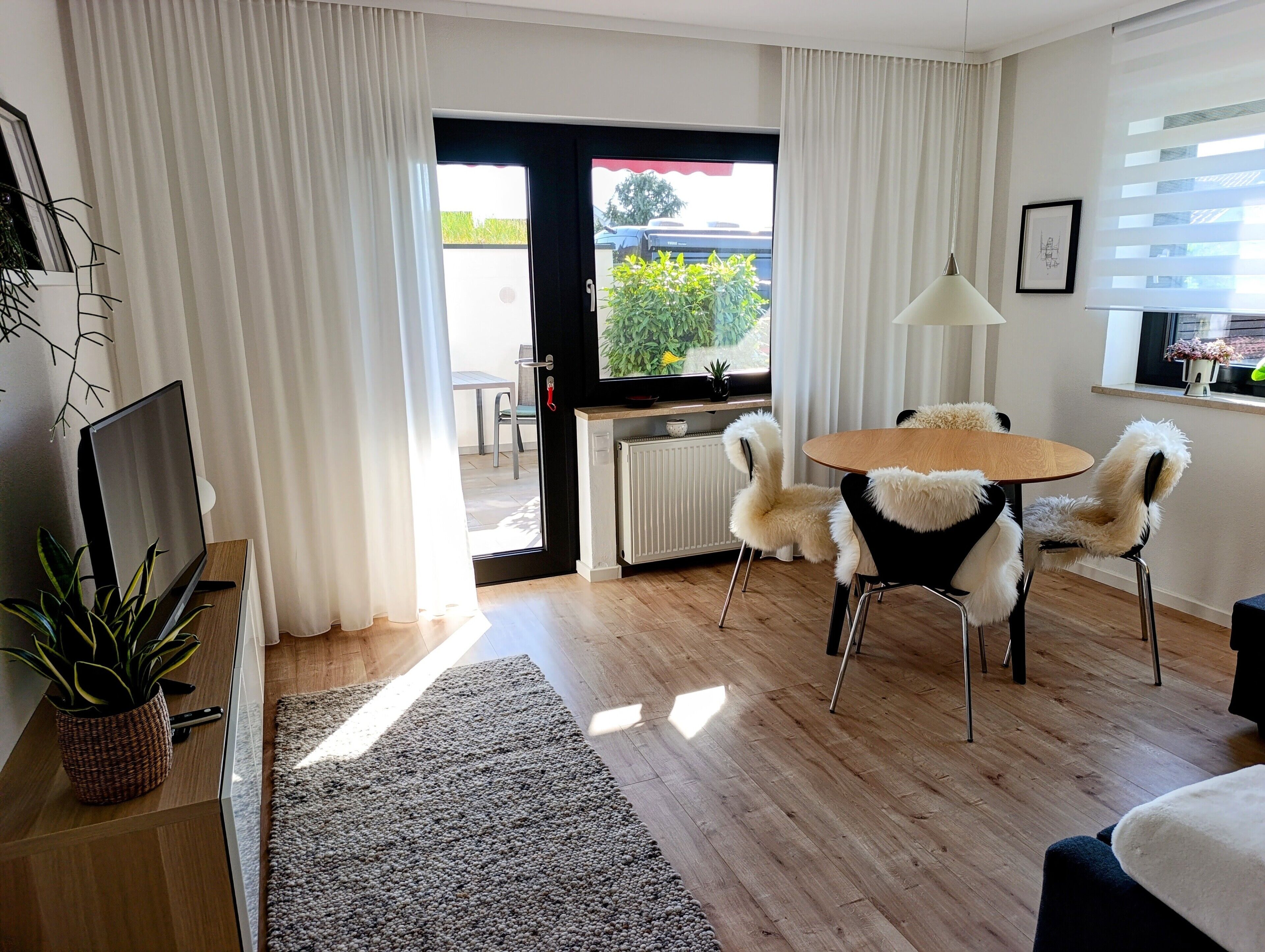 Een moderne woonkamer met een televisie, een eettafel met stoelen, een radiator en een raam met gordijnen.