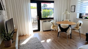 Een moderne woonkamer met een televisie, een eettafel met stoelen, een radiator en een raam met gordijnen.