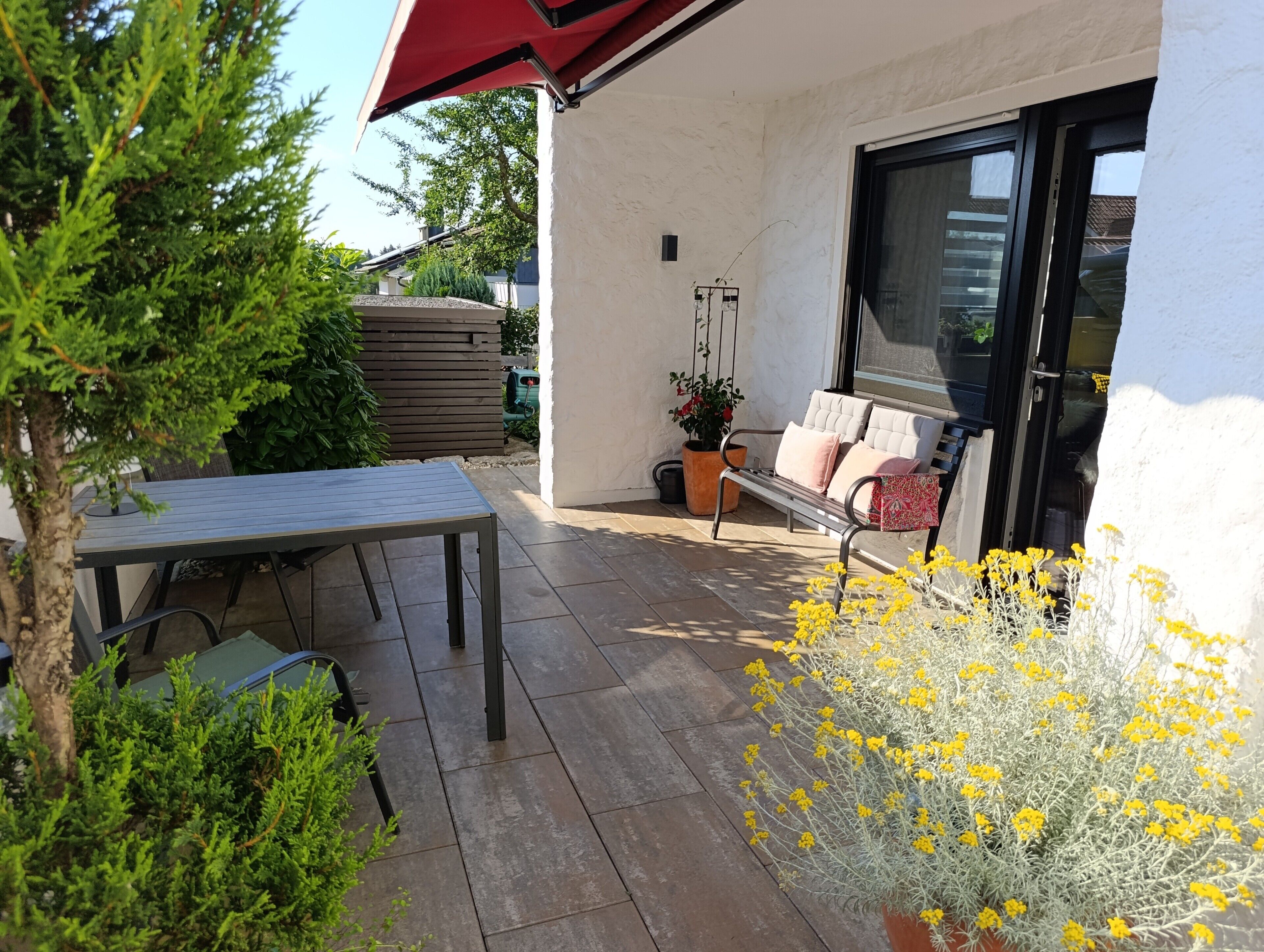 An outdoor patio with a table and chairs, a bench, and potted plants.