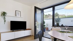 Una sala de estar moderna con un televisor de pantalla plana, una zona de comedor con mesa y sillas, y un ventanal con vistas al exterior.