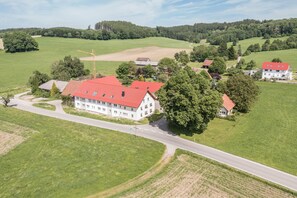 Un grand bâtiment avec un toit rouge, entouré de champs verdoyants et d’arbres.