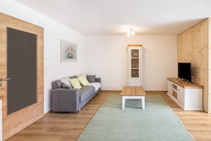 Un salon moderne avec un canapé gris, un meuble en bois, un téléviseur et un tapis vert.