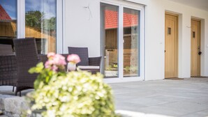 Een modern huis met een terras, schuiframen en een houten deur.