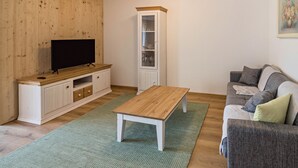 Una sala de estar con televisor, aparador de madera, alfombra verde y sofá gris.